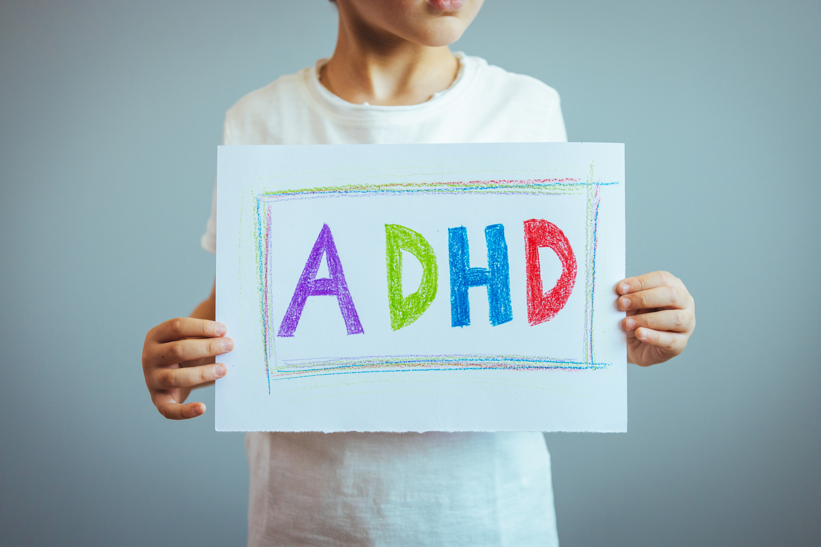 Young boy holds ADHD text written on sheet of paper.